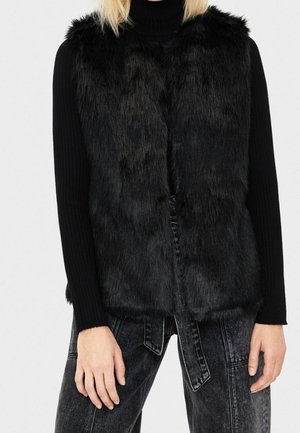 Person wearing a black faux fur vest over a ribbed black long-sleeve top and dark gray high-waisted jeans with wide legs.