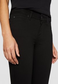 Jeans de mezclilla negra con corte slim, que cuentan con bolsillos delanteros y costuras sutiles. El material tiene una textura suave y un ligero estiramiento.