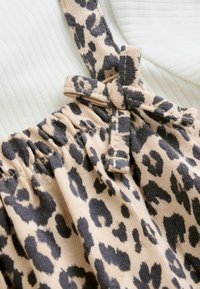 Leoprint-Stoff mit beigem Hintergrund; verfügt über einen geknoteten Träger und eine geraffte Taille. Weiche Textur, gerippter weißer Hintergrund.