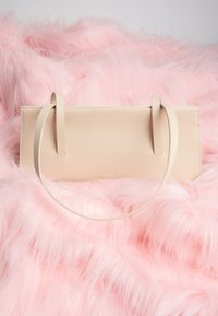 Sac à main rectangulaire en cuir beige avec des fines bretelles reposant sur un tissu doux en fausse fourrure rose.