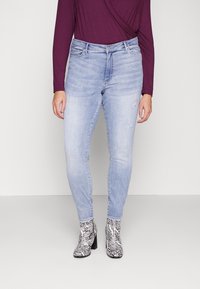 Jeans skinny de un azul claro con un ligero desvanecimiento y detalles desgastados, combinados con una blusa de manga larga de un púrpura intenso y botas con un patrón de cebra en blanco y negro.