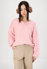 Maglione lavorato a maglia di un rosa pallido con maniche ampie, abbinato a pantaloni beige. Il modello indossa cuffie a forma di orecchie di leopardo marroni. Sfondo neutro.