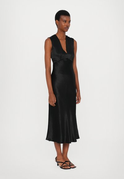 Svart satin klänning med djup V-halsringning, figursydd bodice och fladdrande kjol. Erbjuder en smidig textur och subtil lyster. Matchad med svarta sandaletter med remmar.