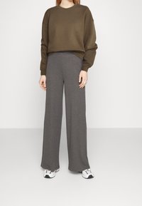 Felpa verde oliva con texture a costine, abbinata a pantaloni larghi grigi scuri a costine. Il modello indossa scarpe da ginnastica bianche.