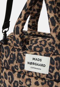 Pohovková taška s leopardím vzorem, černými popruhy a bílou etiketou s nápisem MADS NØRGAARD COPENHAGEN.