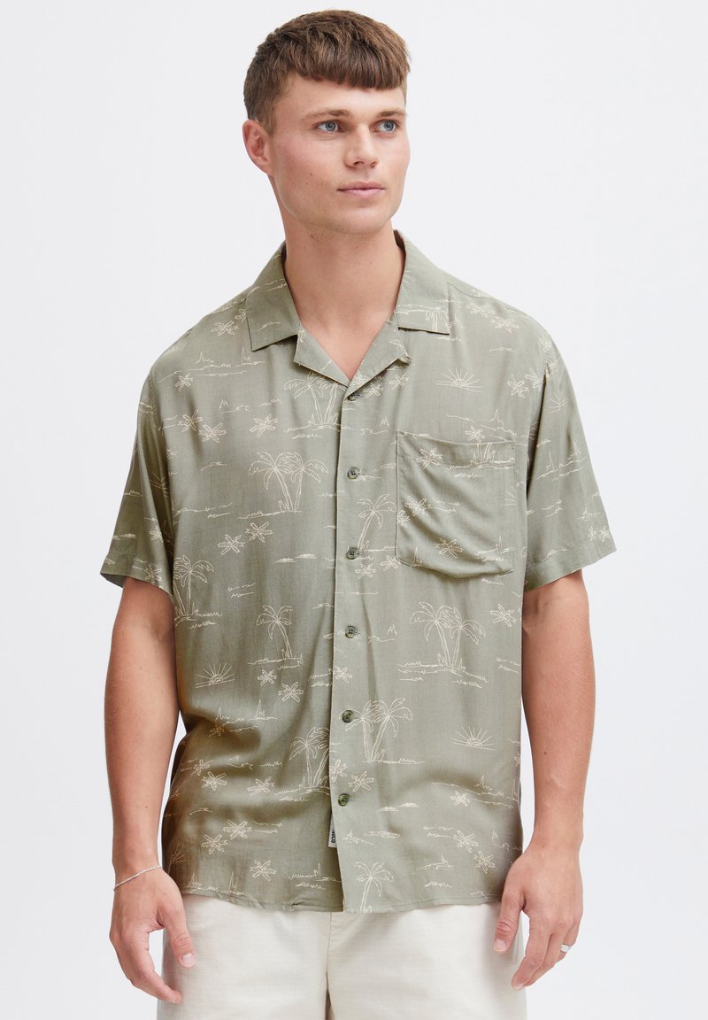 Korte mouwen overhemd in licht olijfgroen, met een palmbomen- en zonpatroon in beige. Inclusief een borstzak en knoopsluiting aan de voorkant.