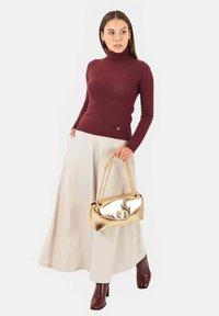 Maglione a collo alto color bordeaux, pantaloni a gamba larga color crema e borsa dorata lucida con tracolla a catena, caratterizzata da una chiusura circolare.