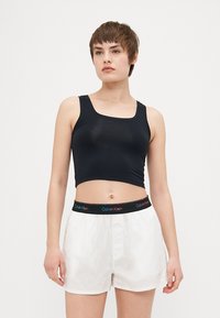 Svart kort topp med fyrkantig halsringning, i kombination med vita shorts med ett flerfärgat "Calvin Klein" resårband.
