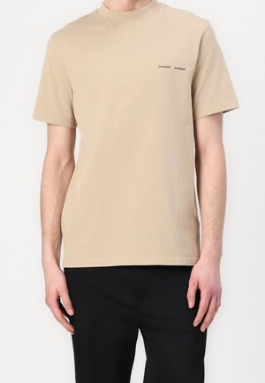 Beige Baumwoll-T-Shirt mit kurzen Ärmeln, Rundhalsausschnitt und einem in Schwarz auf der linken Brust bedruckten Logo. Einfaches Design, lässige Passform.