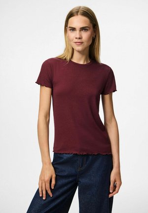 Camiseta corta de manga corta de color burdeos con un escote redondo y un dobladillo con volantes. Hecha de una tela suave, se lleva con jeans de color azul oscuro.