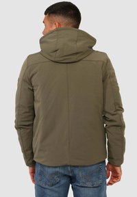 Giacca con cappuccio verde oliva dalla texture liscia, con dettagli di cucitura e silhouette aderente. Vista posteriore che mostra un design minimalista.