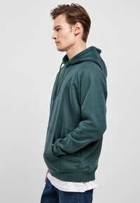 Sudadera con capucha verde hecha de una mezcla de algodón, que cuenta con un bolsillo delantero, capucha ajustable con cordones y puños y dobladillo acanalados.