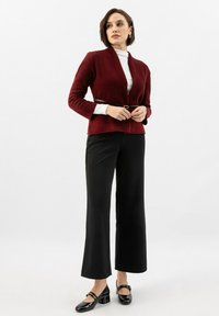 Burgundský přiléhavý blejzr s dlouhými rukávy, v kombinaci s bílým rolákem, černými širokými kalhotami a černými lodičkami se sponou.