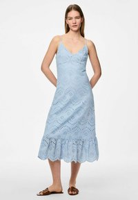 Gaišzila kleita ar pieguļošu augšdaļu, V veida dekoltē un plānām siksnām. Iekļauj acs izgriezumus un viļņotu apakšmalu. Apvienota ar brūnām čībām.