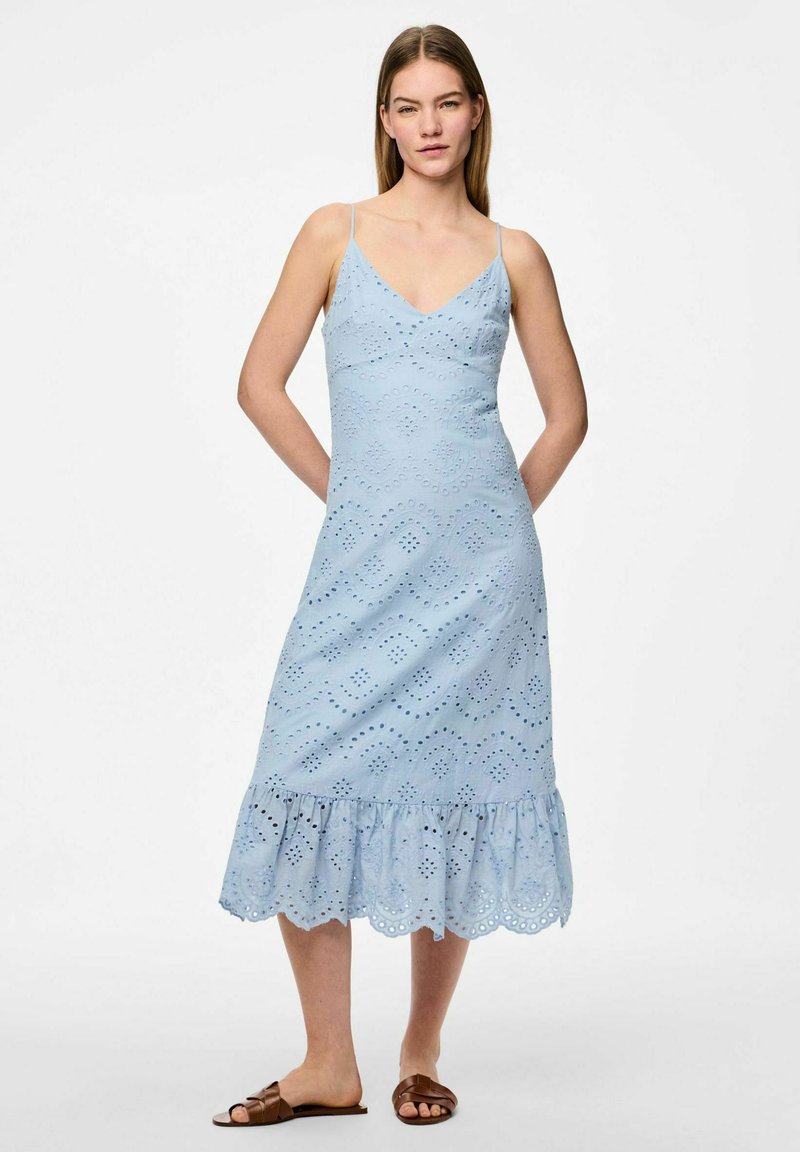 Gaišzila kleita ar pieguļošu augšdaļu, V veida dekoltē un plānām siksnām. Iekļauj acs izgriezumus un viļņotu apakšmalu. Apvienota ar brūnām čībām.