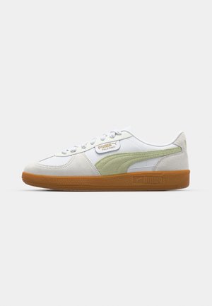 White and green sneakers with suede accents, round toe, and textured gum sole. Features a logo on the side and flat laces.