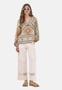 Blusa floral multicolor con escote en V y mangas abullonadas, combinada con pantalones anchos blancos con borde de encaje. Sandalias completan el look.