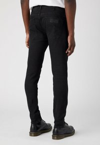 Vaqueros de mezclilla negra con corte slim, diseño de cinco bolsillos y costuras sutiles. Pierna ajustada, textura suave y parche trasero con la marca.