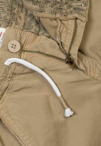 Pantaloni corti beige realizzati in tessuto morbido, con zip, chiusura a bottone, coulisse bianca e vita leggera strutturata.