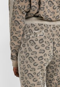 Beige Jogginghosen aus weichem Stoff mit einem subtilen grau Leopardenmuster, slim fit und einem leichten Glanz, mit Taschendetail auf der Rückseite.
