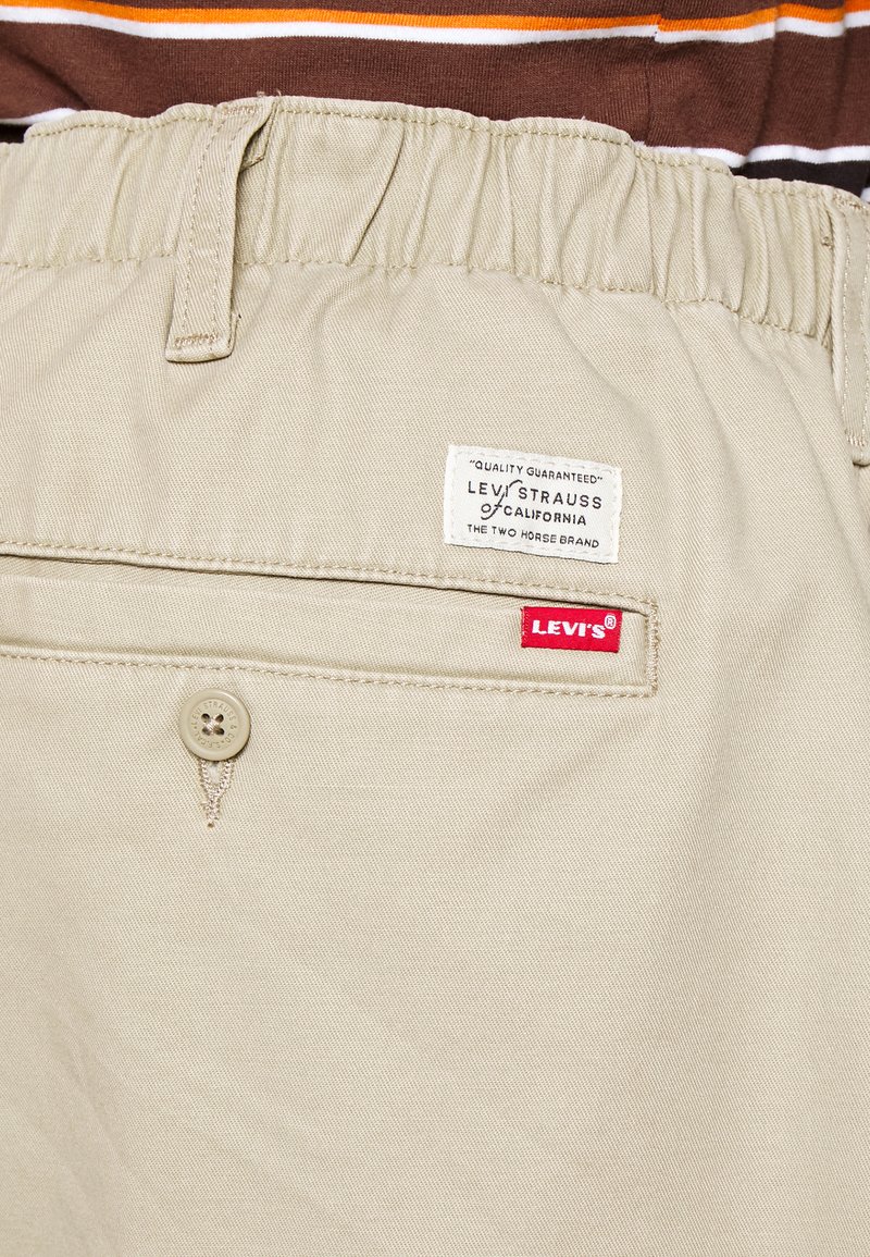 Beige Baumwollshorts mit elastischem Bund, ausgestattet mit einem Levi's Logo-Patch und einer geknöpften Tasche. Strukturierter Stoff mit glatter Oberfläche.