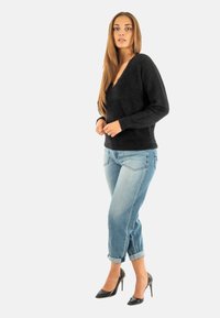 Pull en laine noir avec un décolleté en V, associé à un jean en denim bleu clair retroussé et des chaussures à talons noirs.