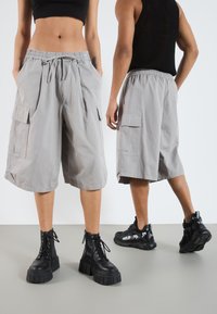 Shorts cargo gris avec un waistband élastique, des plis à l'avant et des poches latérales, associés à des bottes noires à lacets et des baskets noires décontractées.