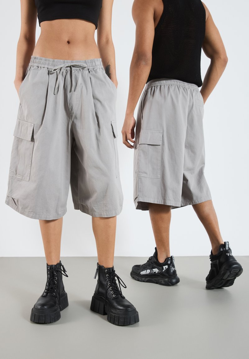 Shorts cargo gris avec un waistband élastique, des plis à l'avant et des poches latérales, associés à des bottes noires à lacets et des baskets noires décontractées.