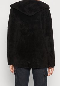 Zwarte fleece jas met een capuchon, zachte textuur, relaxed fit en afgeronde zoom. Geen zichtbare hardware of afwerking.