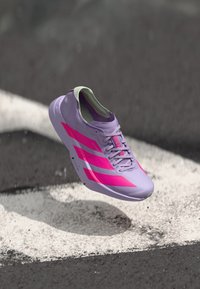 Helllila Laufschuh mit pinken Streifen und Akzenten, der ein schlankes Design, eine strukturierte Oberseite und einen gepolsterten Kragen aufweist. Schwebt über einer Oberfläche.
