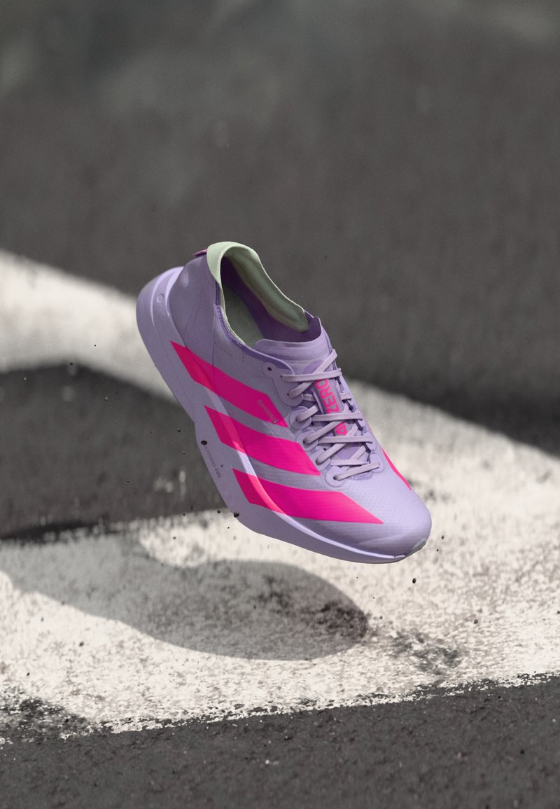 Helllila Laufschuh mit pinken Streifen und Akzenten, der ein schlankes Design, eine strukturierte Oberseite und einen gepolsterten Kragen aufweist. Schwebt über einer Oberfläche.