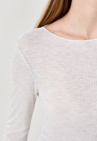 Jasnoszary longsleeve z teksturowanej, prążkowanej tkaniny z szerokim dekoltem. Odsłania szczegóły ramion i obojczyka.