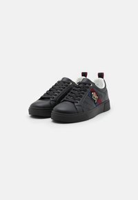 Svarte lær sneakers med mønstrete overflate, rund tå og snøredesign. Har gulløyer og en flerfarget logo-patch på siden.