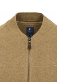Khakifarbener Reißverschluss-Pullover mit geripptem Kragen und Bündchen, strukturiertem Strickstoff, einem blauen Etikett am Hals und einem braunen Reißverschluss-Zug.