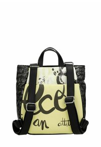 Bolsa tote negra y amarilla que combina diferentes texturas, con letras llamativas, correas ajustables y dos asas superiores. Presenta elementos de diseño abstracto.