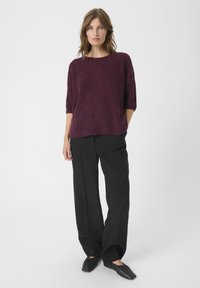 Bordowy sweter dziany z krótkimi rękawami, o luźnym kroju, w połączeniu z czarnymi spodniami z wysokim stanem i czarnymi płaskimi butami. Minimalistyczny design.