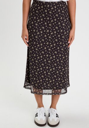 Jupe midi noire avec un motif floral, fabriquée en tissu léger, translucide à l'ourlet, assortie à des baskets blanches et un haut décontracté.