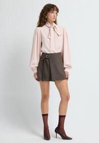 Blusa rosa clara con lazo, mangas abullonadas; minifalda marrón con pliegues y un lazo lateral con un acento dorado circular; calcetas de color burdeos transparentes; tacones altos.