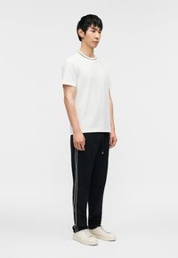 Λευκό κοντομάνικο μπλουζάκι με αντίθετο μαύρο γιακά, συνδυασμένο με μαύρο παντελόνι φόρμας με λευκές λωρίδες στο πλάι και ανοιχτόχρωμα αθλητικά παπούτσια.