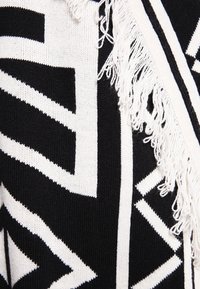 Poncho de punto en blanco y negro con patrones geométricos, que presenta flecos texturizados a lo largo de los bordes.