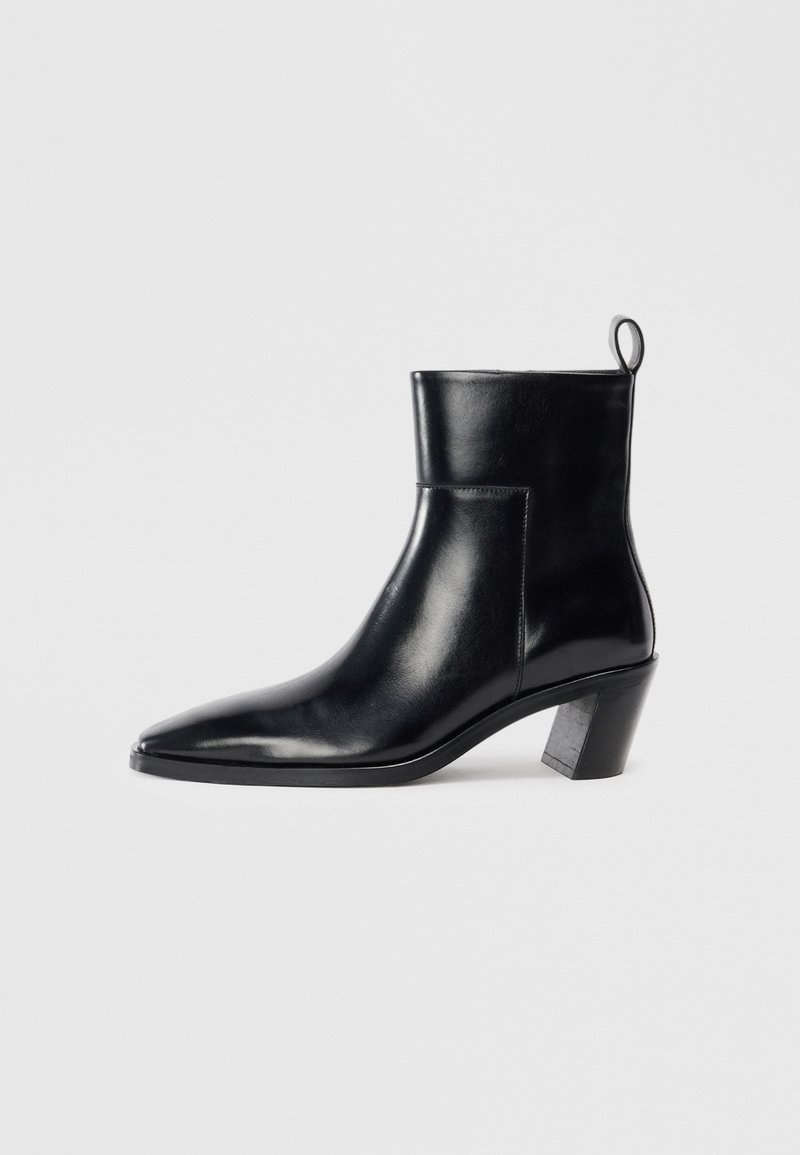 Cizme negre din piele până la gleznă, cu vârful ascuțit, toc geometric patrulat și un manșon pentru tragere în spate. Textură netedă și design elegant.