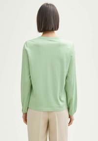 Chemise à manches longues vert clair avec des rayures verticales, en tissu doux, col rond et coupe décontractée, associée à un pantalon beige.