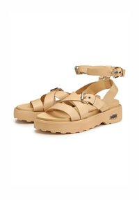 Sandali in pelle beige con fasce incrociate, fibbie regolabili sulla caviglia e suole in gomma spesse con texture rigata. Accentuati da accessori metallici.