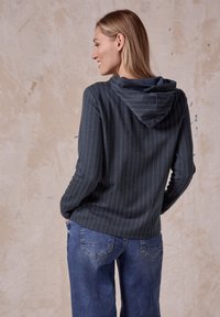 Dunkelblau gestreifter Hoodie mit rundem Ausschnitt, aus weichem Material und lässigem Schnitt. Kombiniert mit lockeren Jeans.