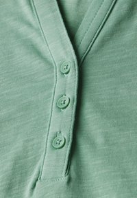 Camicia in cotone verde con tessuto texturizzato, abbottonatura con quattro bottoni verdi e scollo a V.