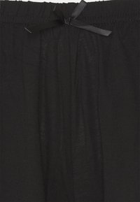 Black fabric pants with a gathered waist and a bow accent. Smooth texture with vertical pleats and an elastic waistband.