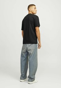Camiseta de algodón negra y jeans holgados de un azul claro. El conjunto presenta un ajuste relajado, un diseño minimalista y zapatillas blancas.