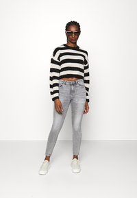 Pull court à rayures noires et blanches, jean skinny gris et baskets blanches. Le modèle porte des lunettes de soleil noires ; textures de tricot lisse et de denim.