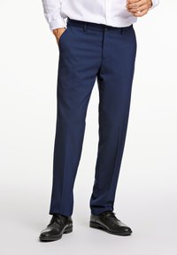 Pantalones de vestir azul marino con corte recto, frontal plano, bolsillos y textura suave. Combinados con zapatos de vestir negros.