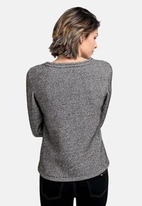 Schwarzer und weißer, Fischgrätenmuster Pullover, runder Halsausschnitt, lange Ärmel, weicher Stoff, figurnah geschnitten, getragen mit schwarzen Hosen.